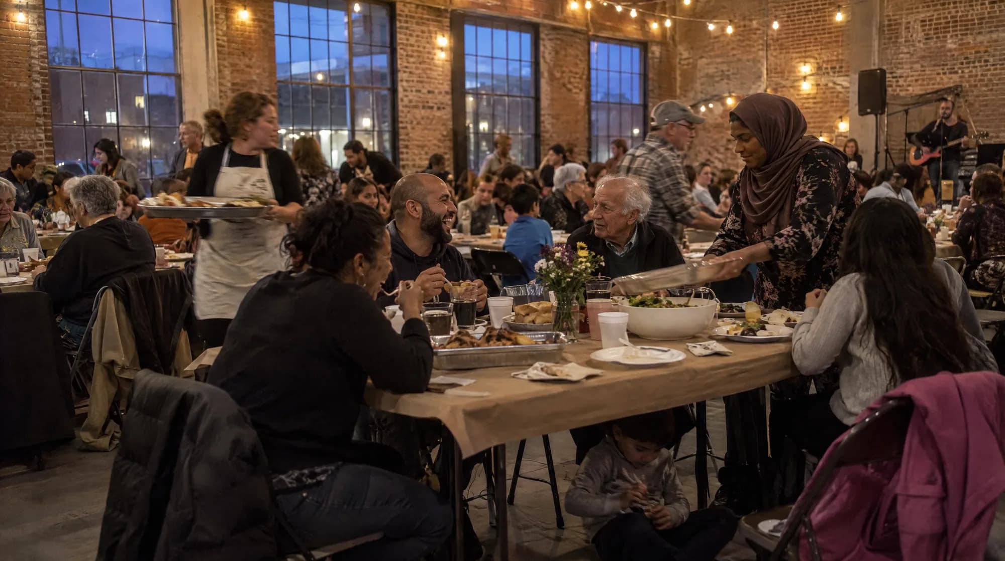 Families sharing a meal at long tables in a hall strung with lights