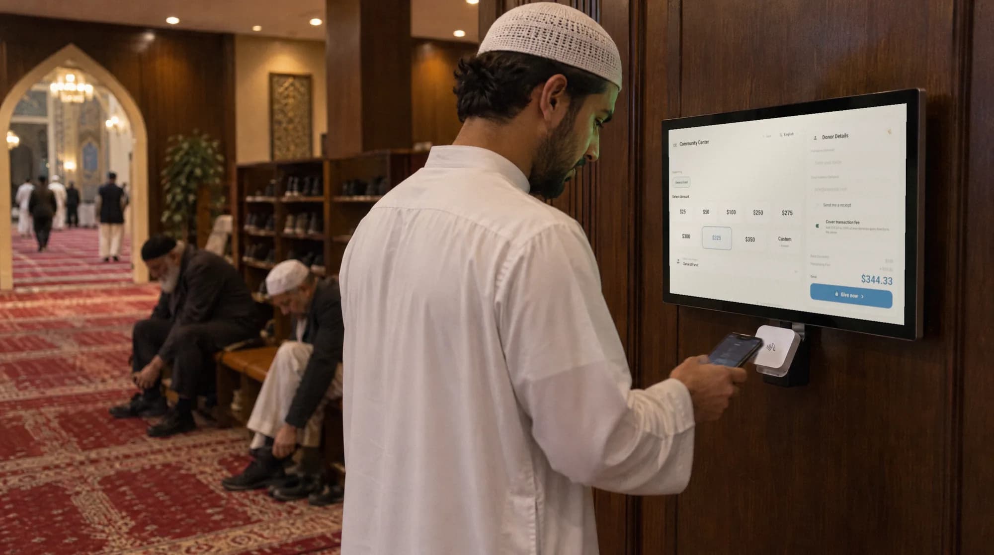 A man taps his phone on a wall-mounted donation kiosk in a wood-paneled masjid hallway